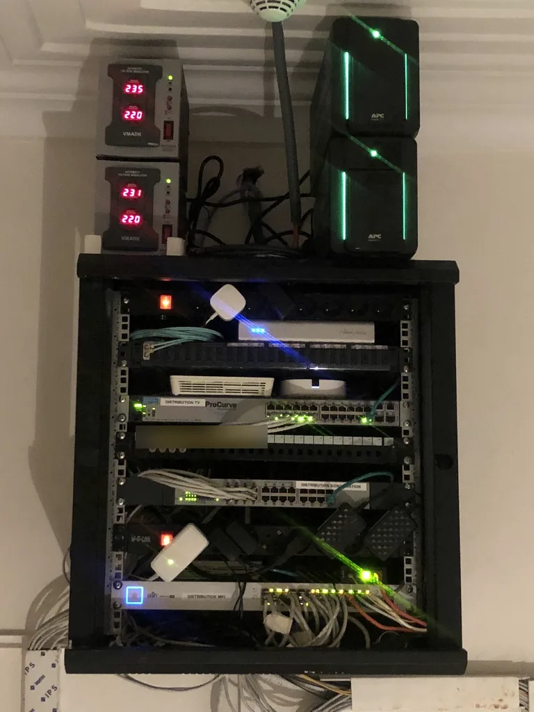 Villa, baie de distribution. Un switch par usage, étiqueté Wi-Fi, télévision et sonorisation. Onduleurs et régulateurs de tension au-dessus de la baie.